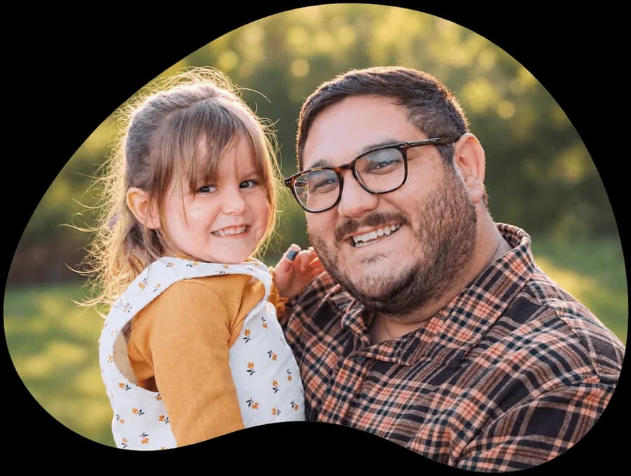 A smiling dad holding his young daughter outdoors